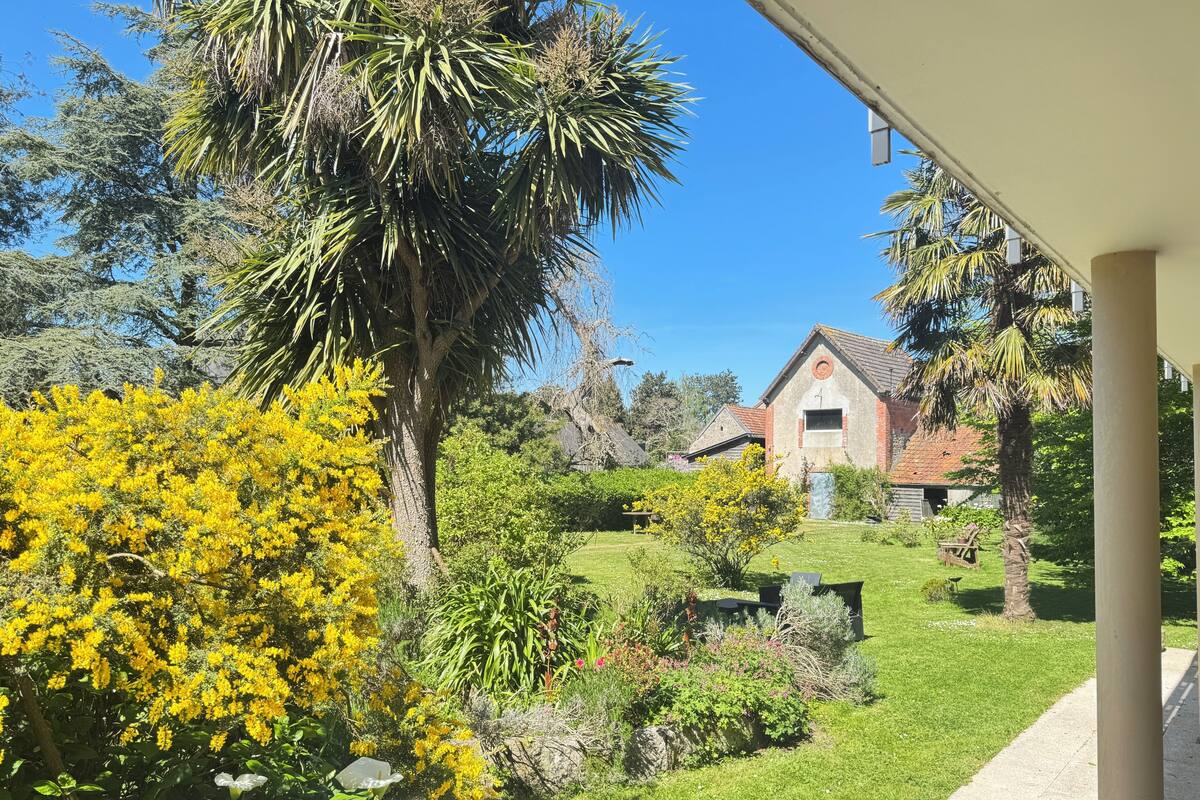 Una casa con fachada de ladrillo rojo, rodeada de un jardín bien cuidado con plantas variadas y césped.