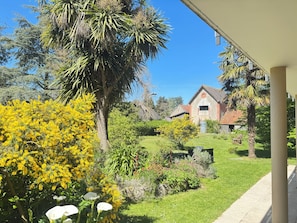 Uma casa com fachada de tijolos vermelhos, rodeada por um jardim bem cuidado com diversas plantas e gramado.