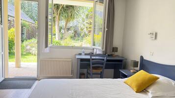 Une chambre à coucher comprenant un lit, un bureau, une chaise, une fenêtre avec des rideaux et une vue sur la verdure à l’extérieur.
