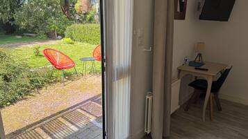 Een kamer met een schuifdeur naar een tuin, een kleine tafel met stoel, een radiator en een aan de muur bevestigde televisie.