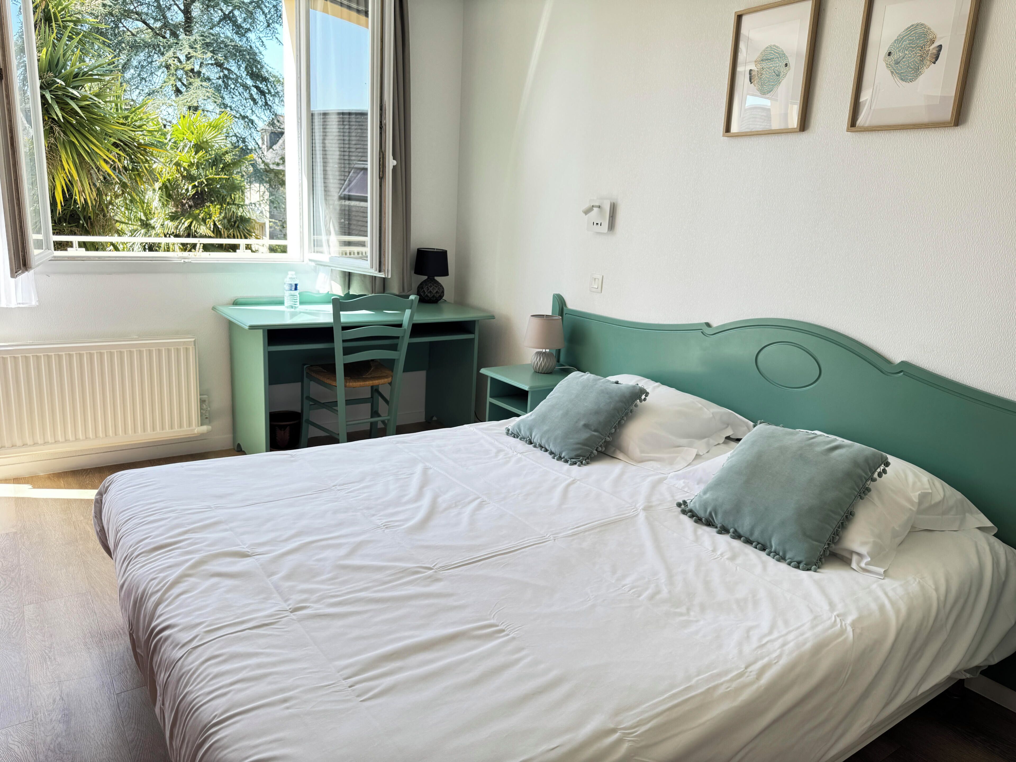 A bedroom with a bed, desk, chair, and a window with a view of trees.
