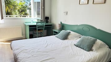 Quarto com cama, escrivaninha, cadeira e janela com vista para árvores.