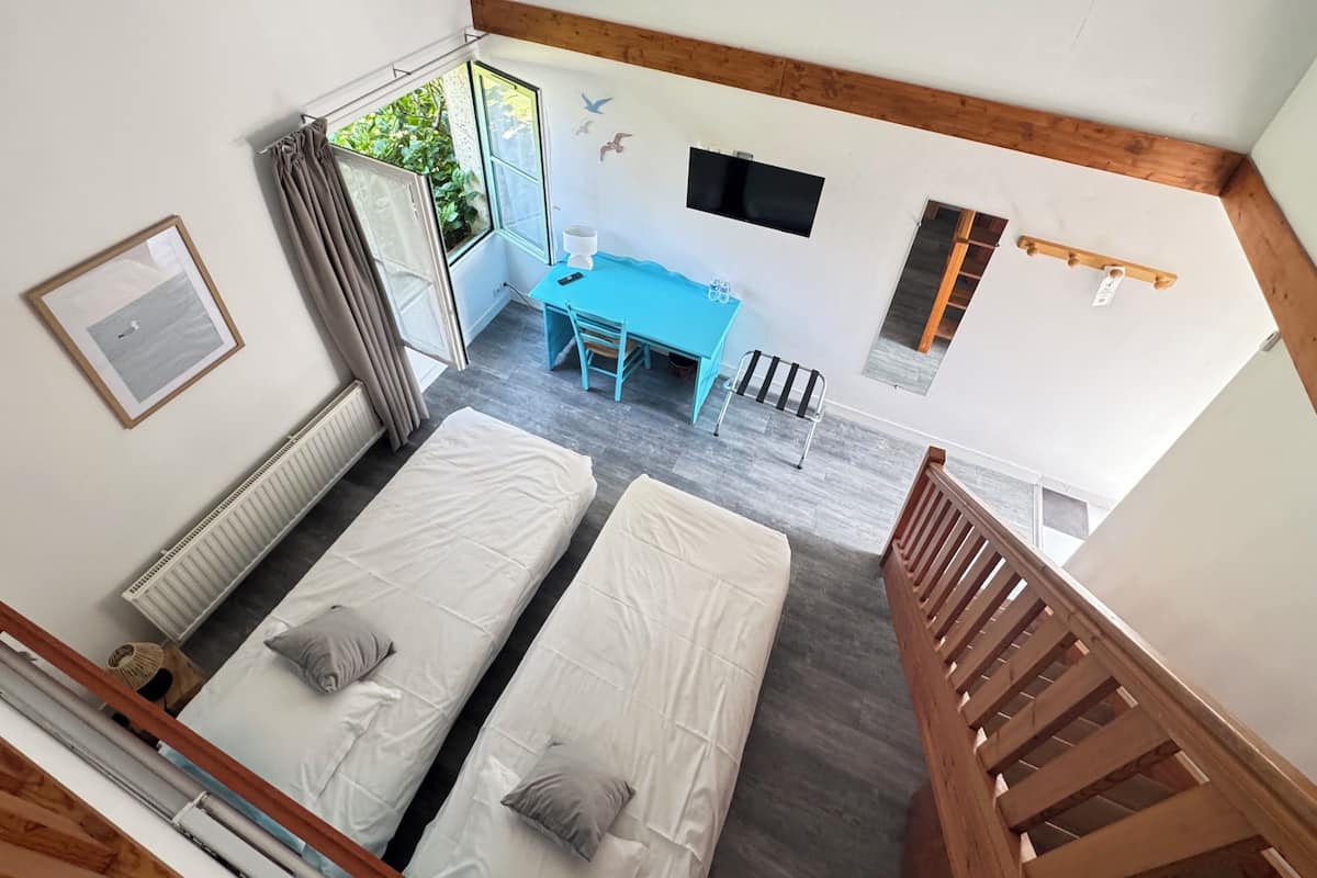 Una habitación con dos camas, un escritorio, una ventana con cortinas, un televisor y una escalera de madera.