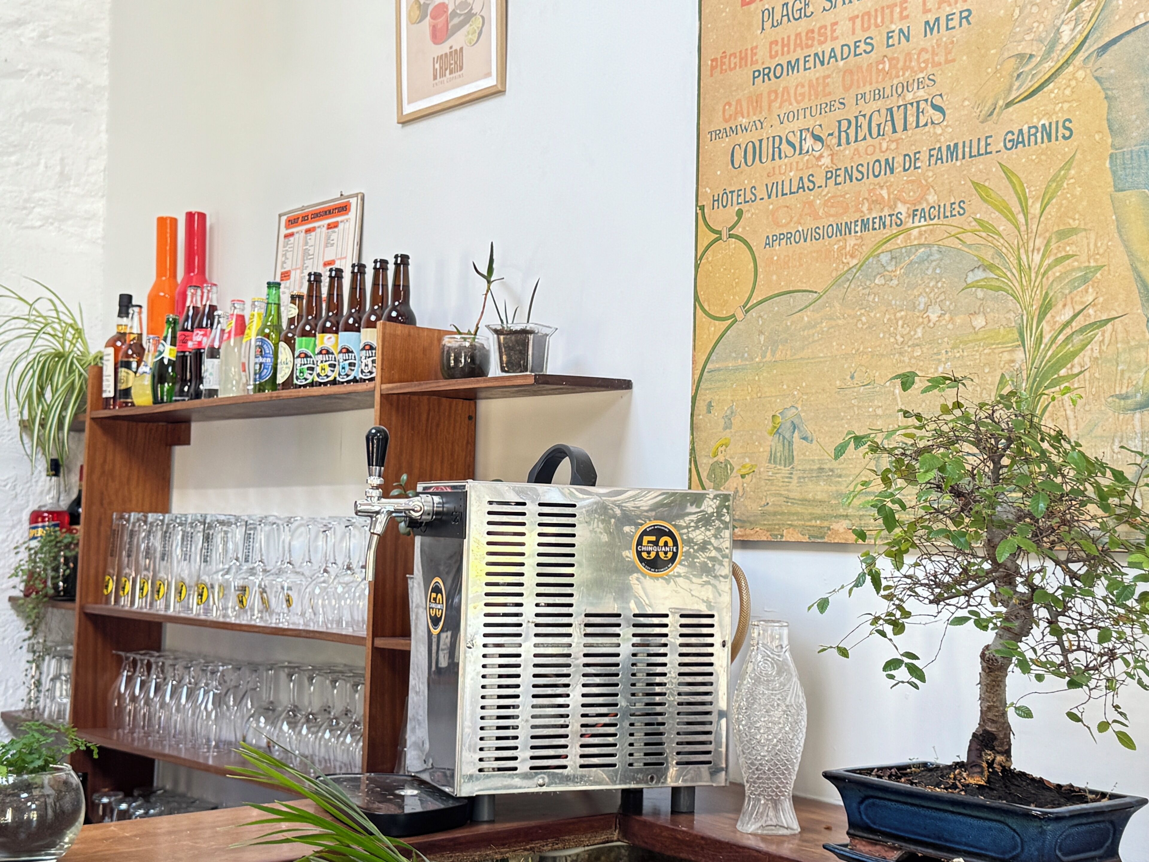A bar area with a beer tap, shelves with bottles, glasses, and a poster on the wall.