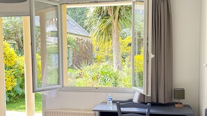 A room with a bed, a desk with a chair, a window with curtains, and a radiator. - La Demeure Du Perron (Quettehou)