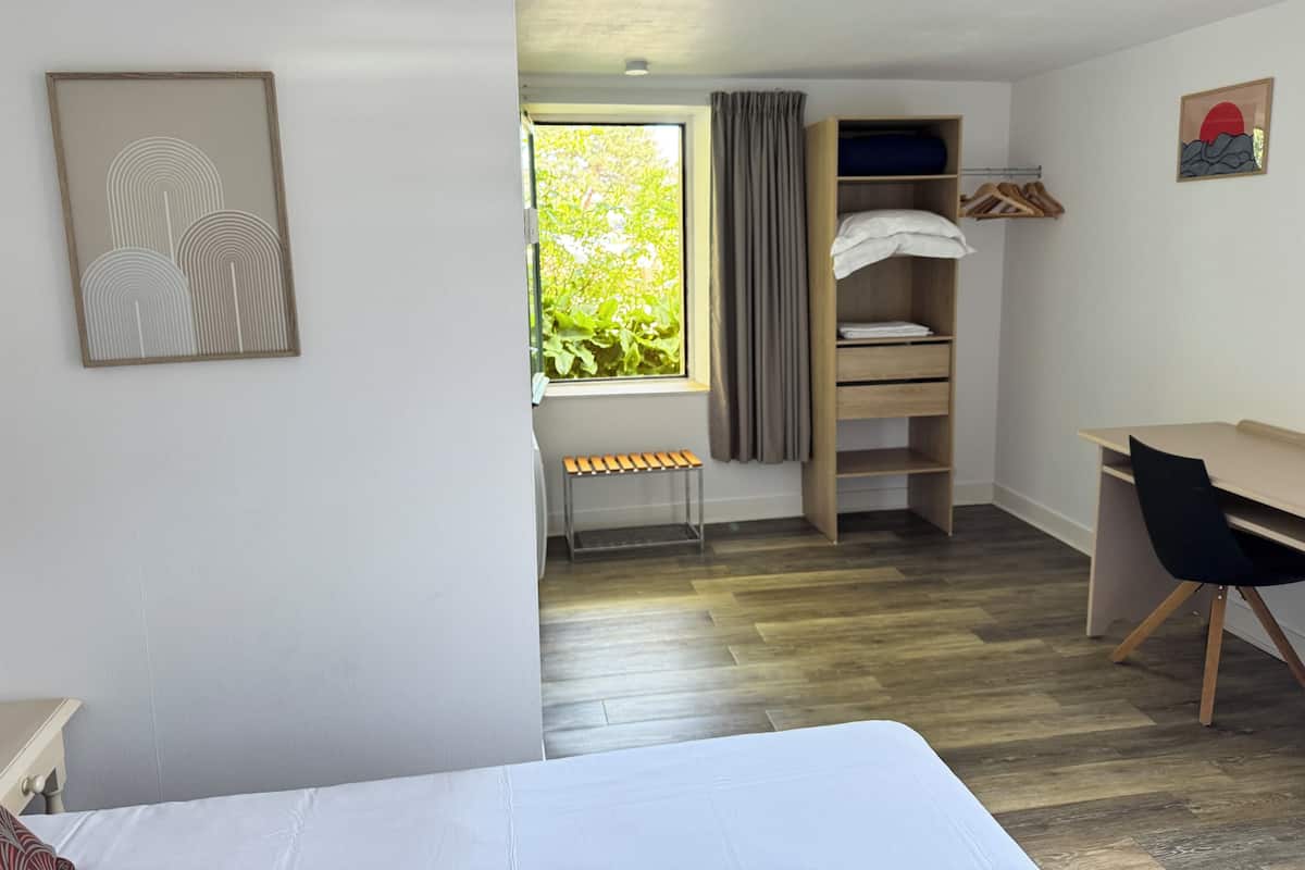 Un dormitorio con cama, escritorio, silla, armario y ventana con cortinas.