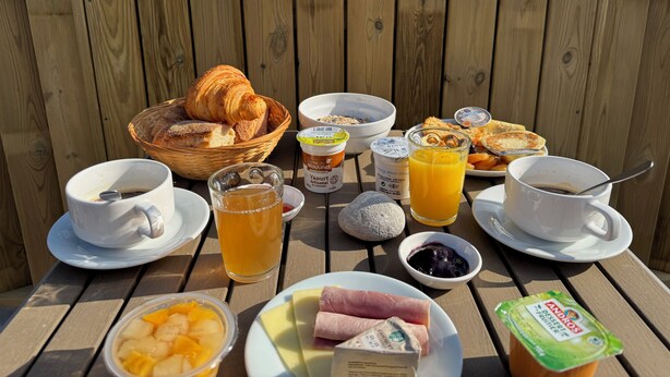 A breakfast setup with croissants, bread, yogurt, juice, and fruit on an outdoor table. - La Demeure Du Perron (Quettehou)