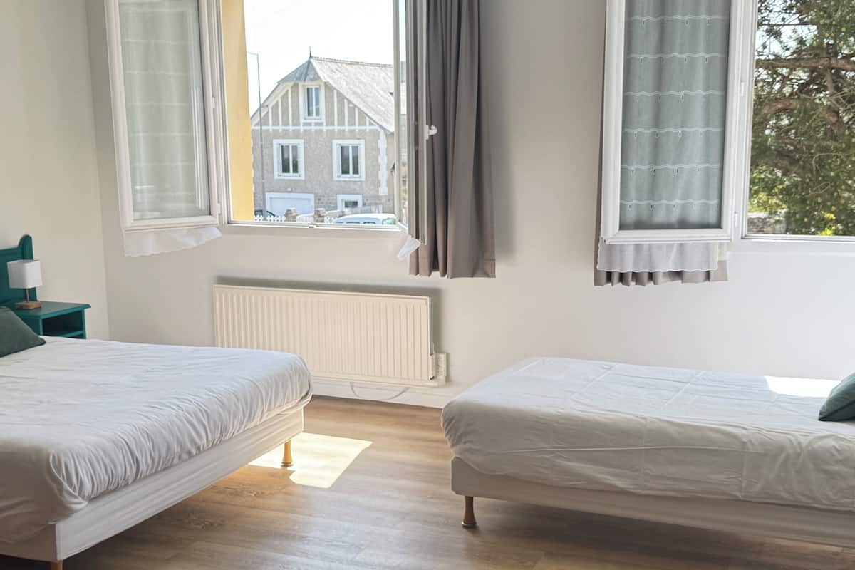 Un dormitorio con dos camas, una ventana con cortinas, un radiador y vistas a un edificio.