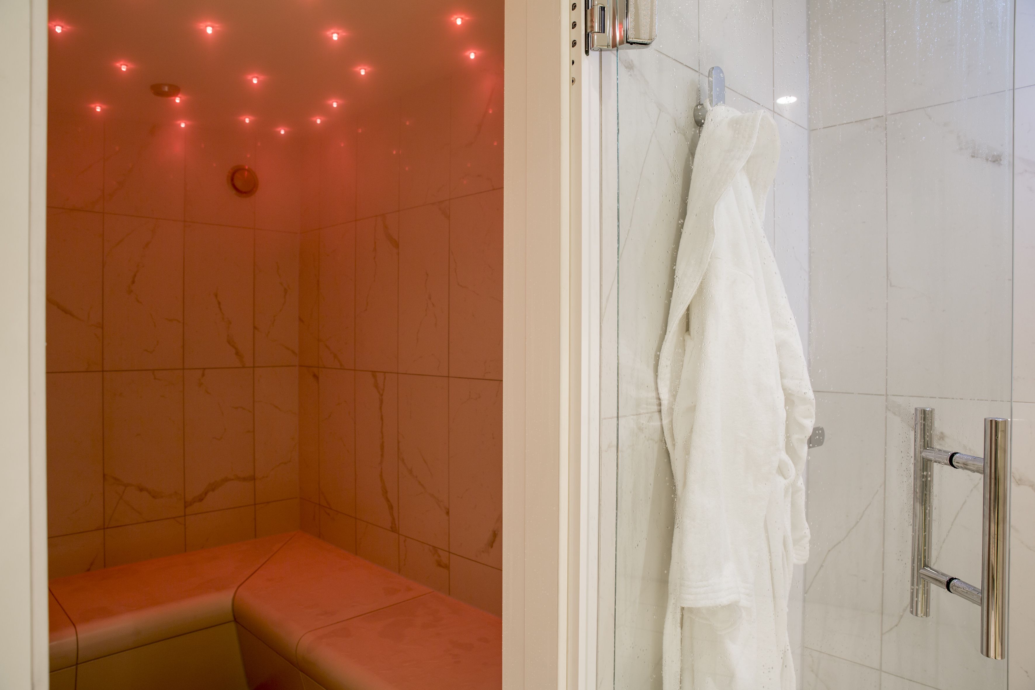 A bathroom with a marble wall, a bench, a towel rack, and a shower area.