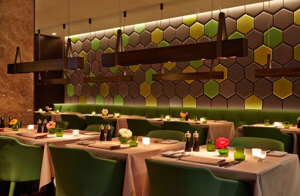 Un restaurante con asientos y mesas verdes, paneles hexagonales en la pared y lámparas colgantes.