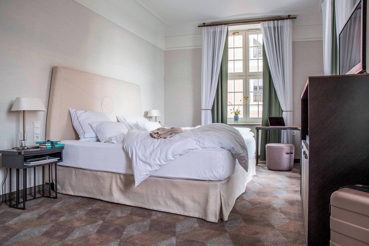 Habitación de hotel con una cama grande, mesitas de noche, un escritorio, una silla, una ventana con cortinas y un televisor.