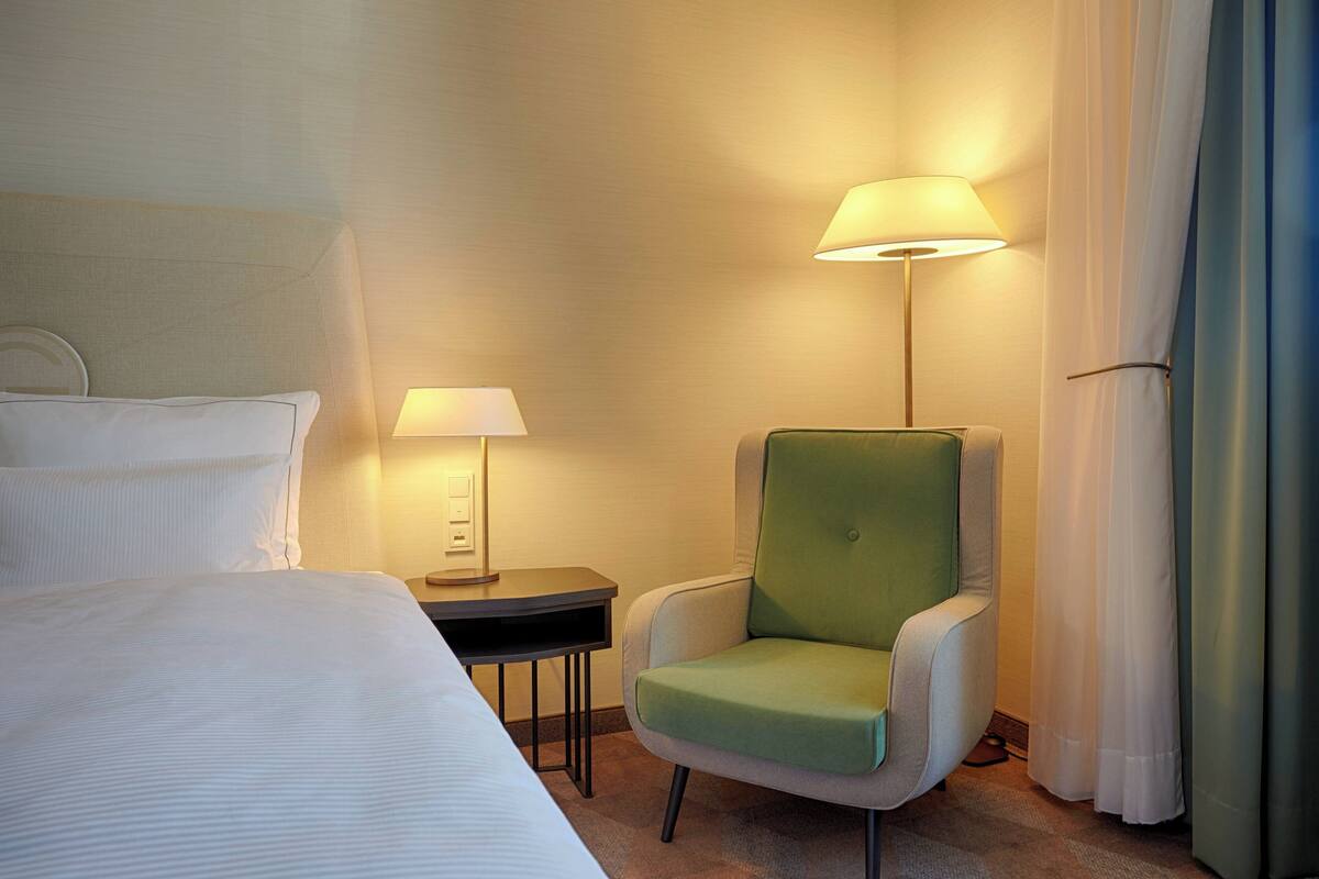 A hotel room with a bed, a chair, a desk, and a lamp.