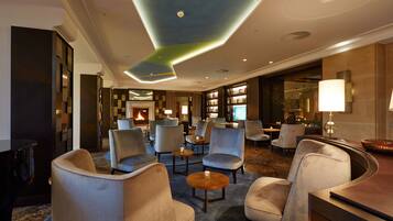 A modern hotel lobby with seating areas, a fireplace, and a well-lit ceiling.