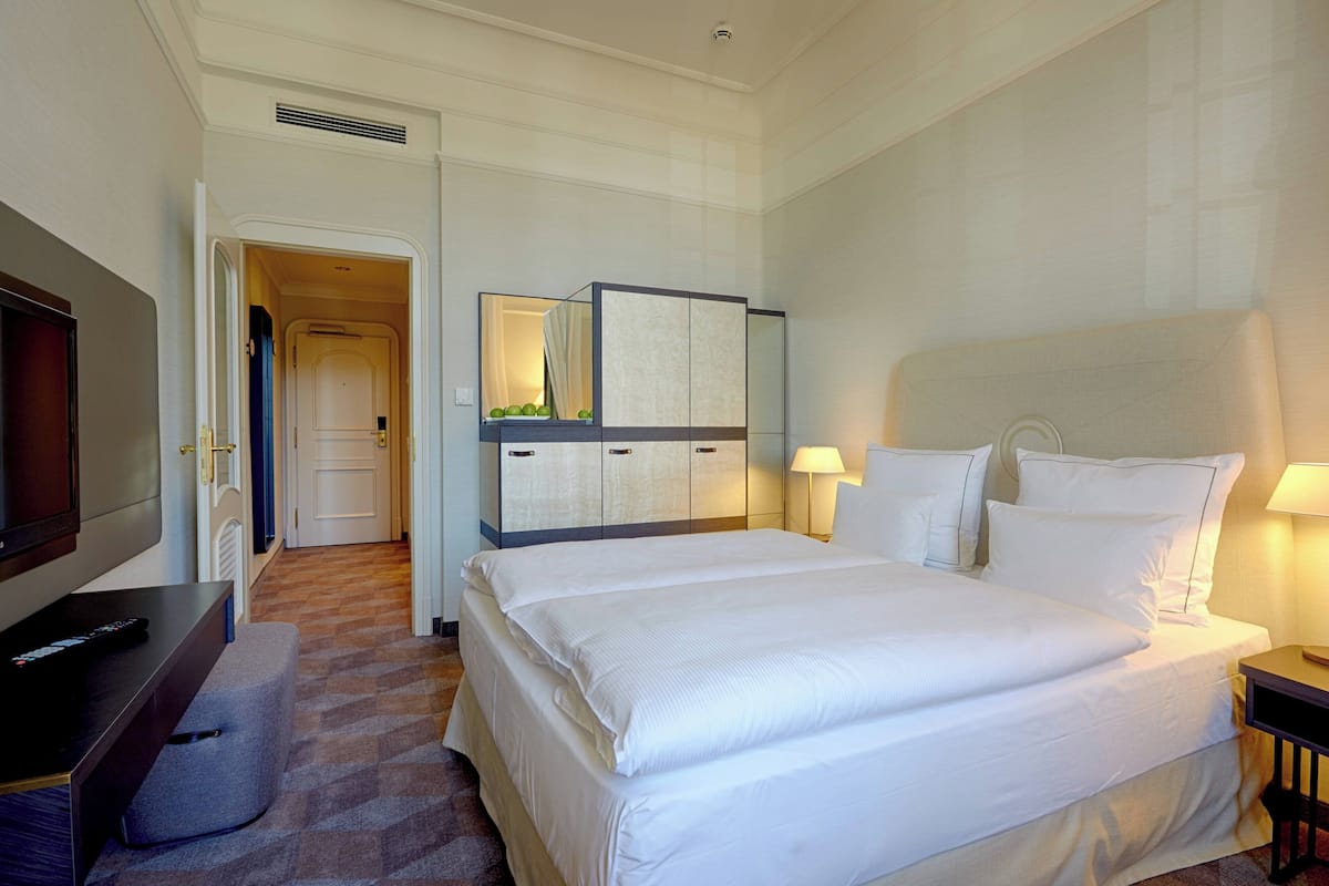 A hotel room with a large bed, a television, a desk, and a wardrobe.