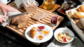 Une table dressée pour le petit-déjeuner, avec du pain, des croissants et diverses confitures sur une planche en bois.