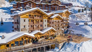 Un chalet en bois à plusieurs étages, doté de balcons, d'un télésiège et d'une terrasse en bois avec des sièges extérieurs.