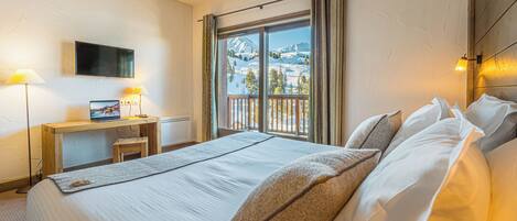 Una habitación de hotel con cama, escritorio con una computadora portátil, televisión y ventana con vista a la montaña.
