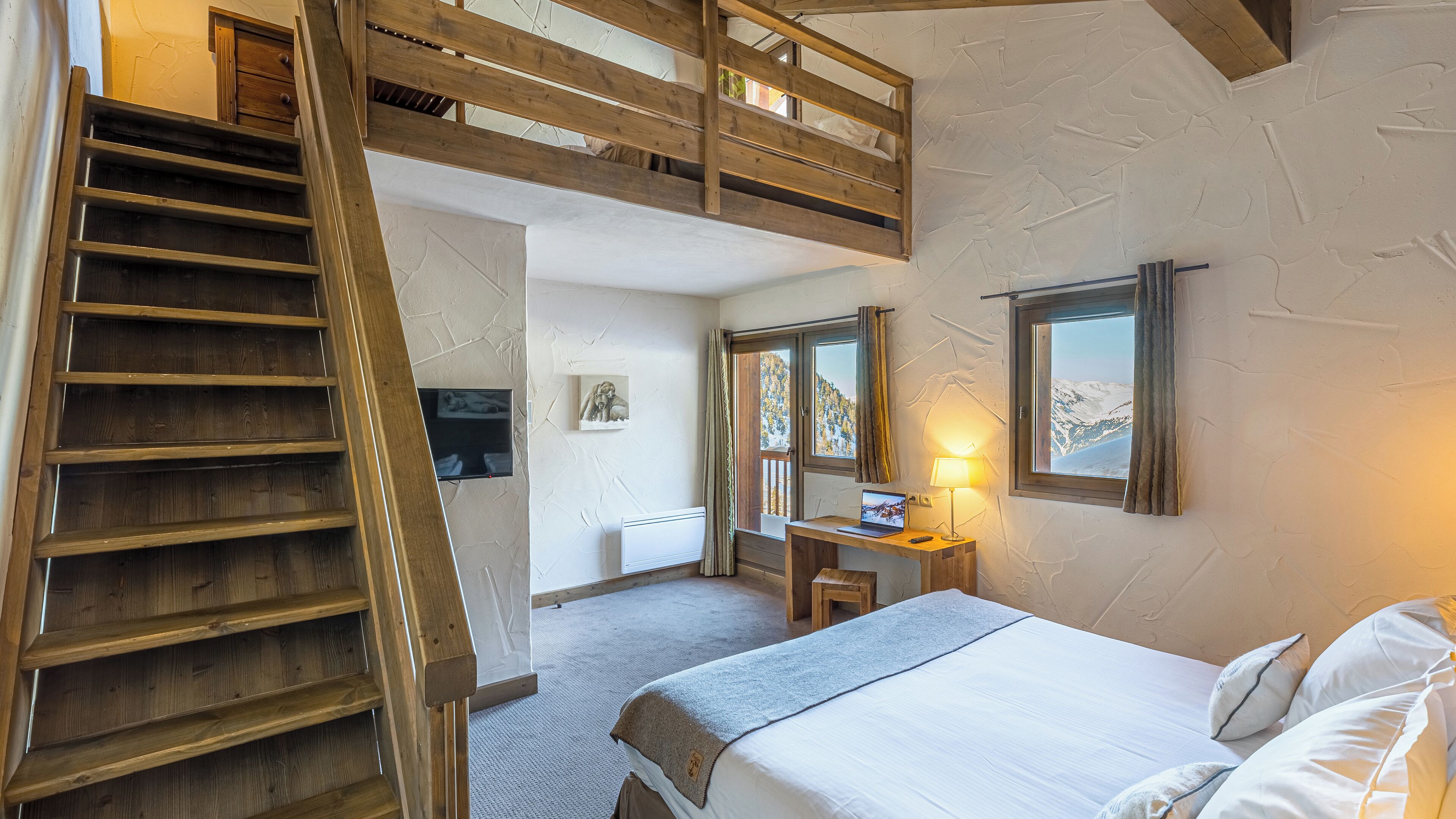 Ein Schlafzimmer mit Etagenbett, Schreibtisch, Computer, Lampe und Fenster mit Blick auf die Berge.