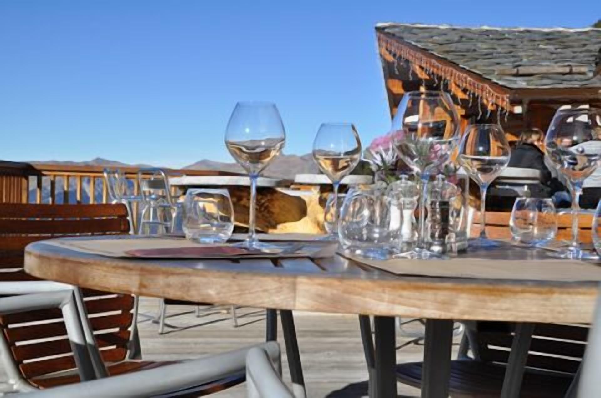 A table set for dining with wine glasses and a vase of flowers, overlooking a mountainous landscape.