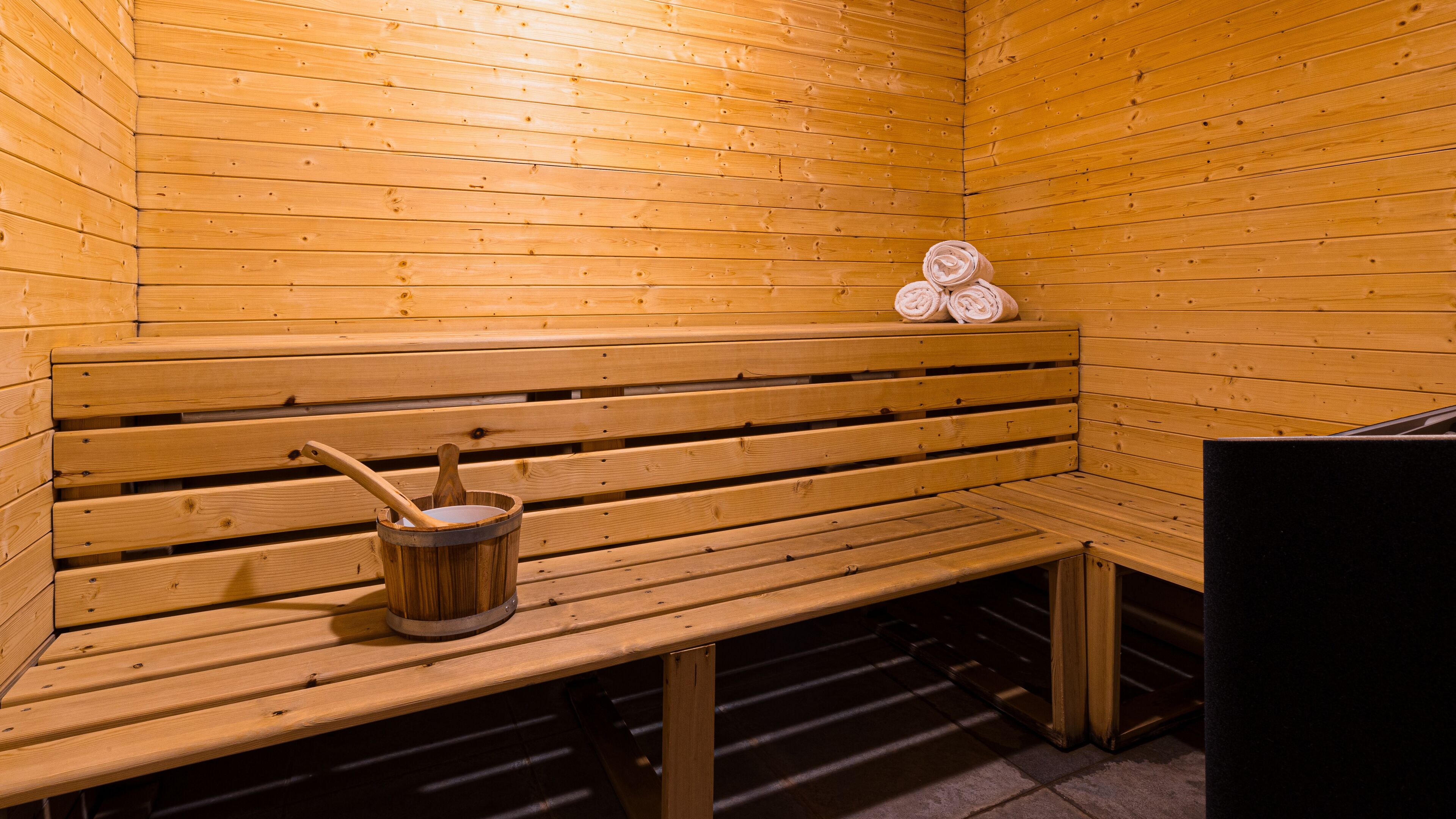 A wooden sauna with benches and a bucket with a wooden mallet.