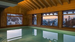 Une pièce dotée d’une grande piscine à débordement dont les parois vitrées reflètent le paysage montagneux enneigé.