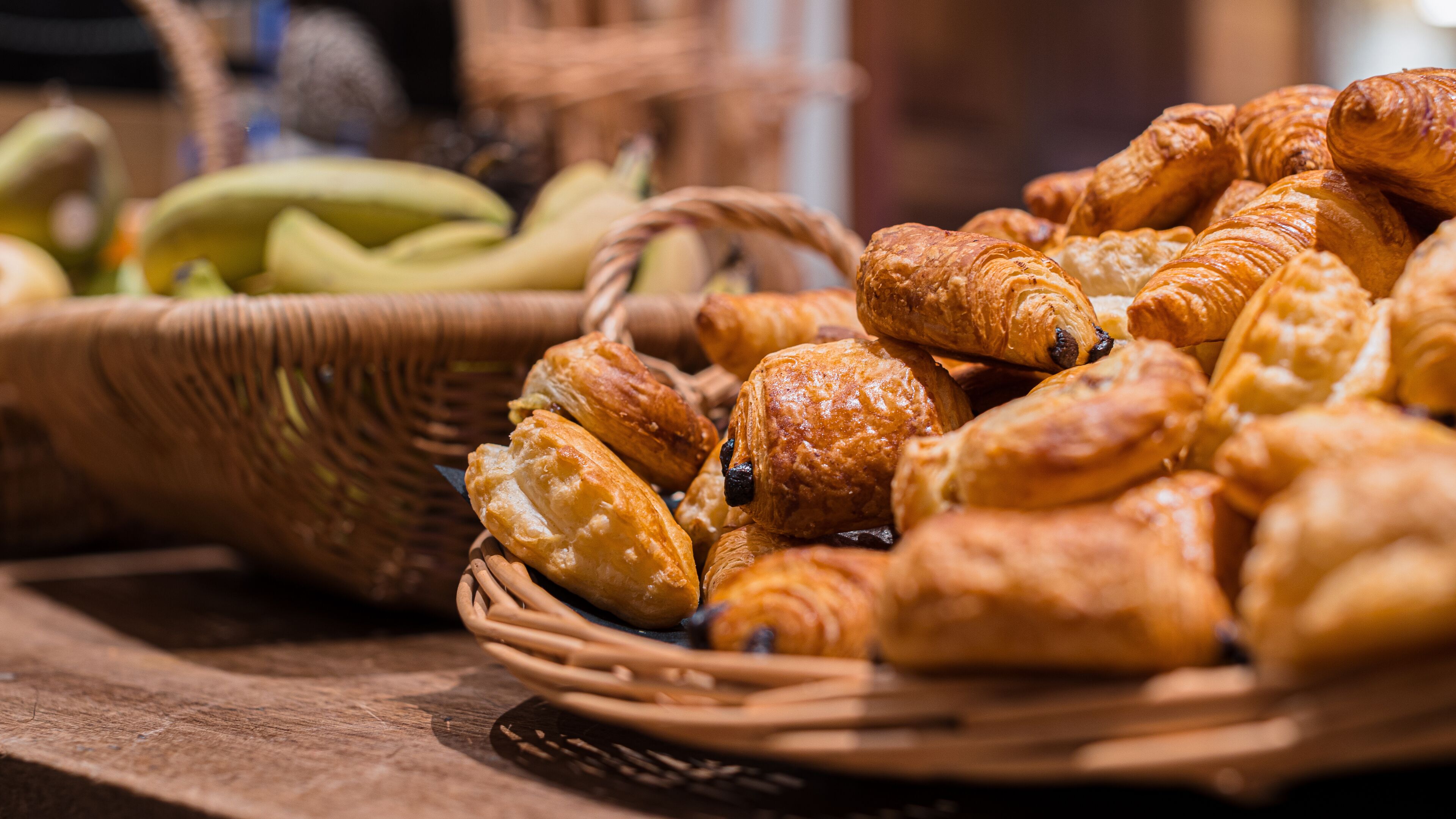 Ein Korb mit Croissants und ein Korb mit Bananen auf einem Holztisch.