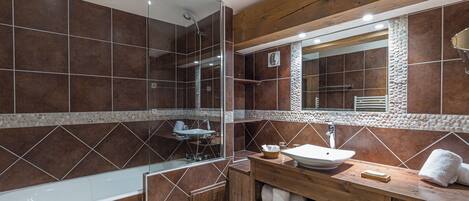 Un baño con cabina de ducha de vidrio, tocador de madera con lavamanos y espejo sobre el tocador.