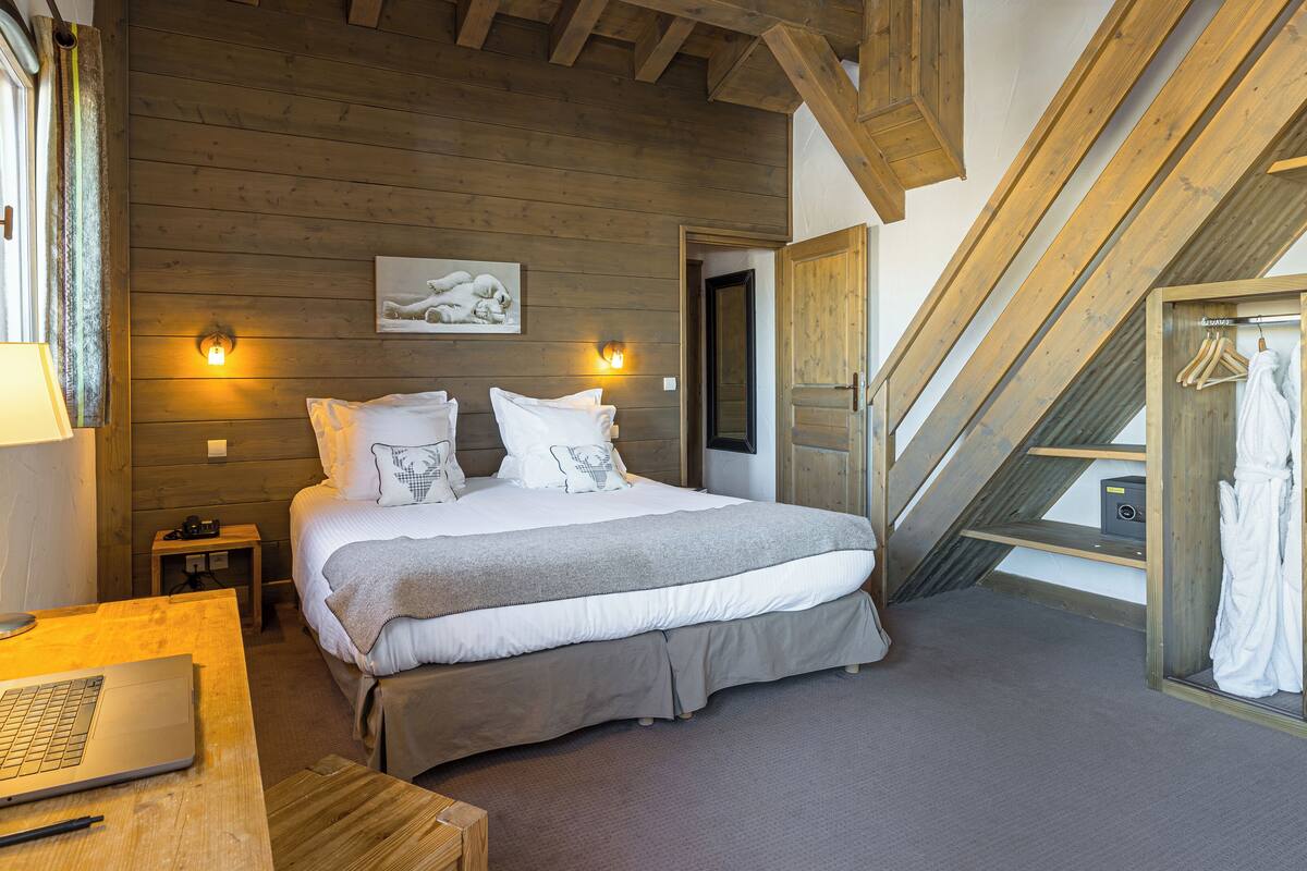 A bedroom with a bed, bedside table, lamp, laptop, and a view of the outside.