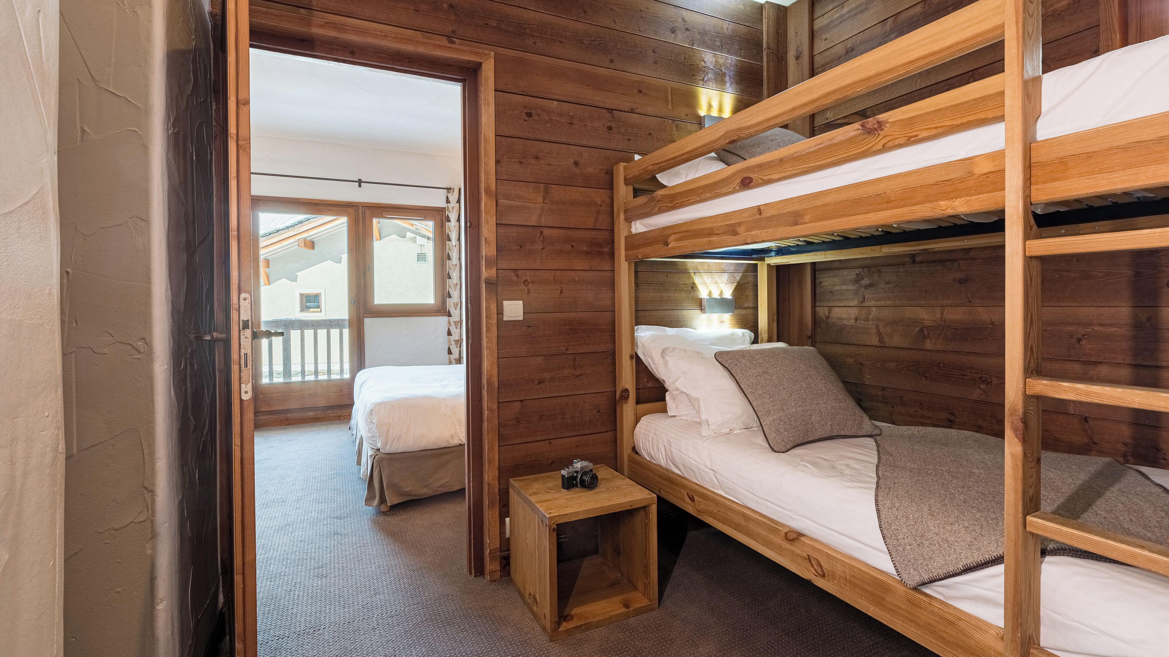 Une chambre avec un lit superposé en bois, une petite table de chevet en bois et un appareil photo posé dessus.