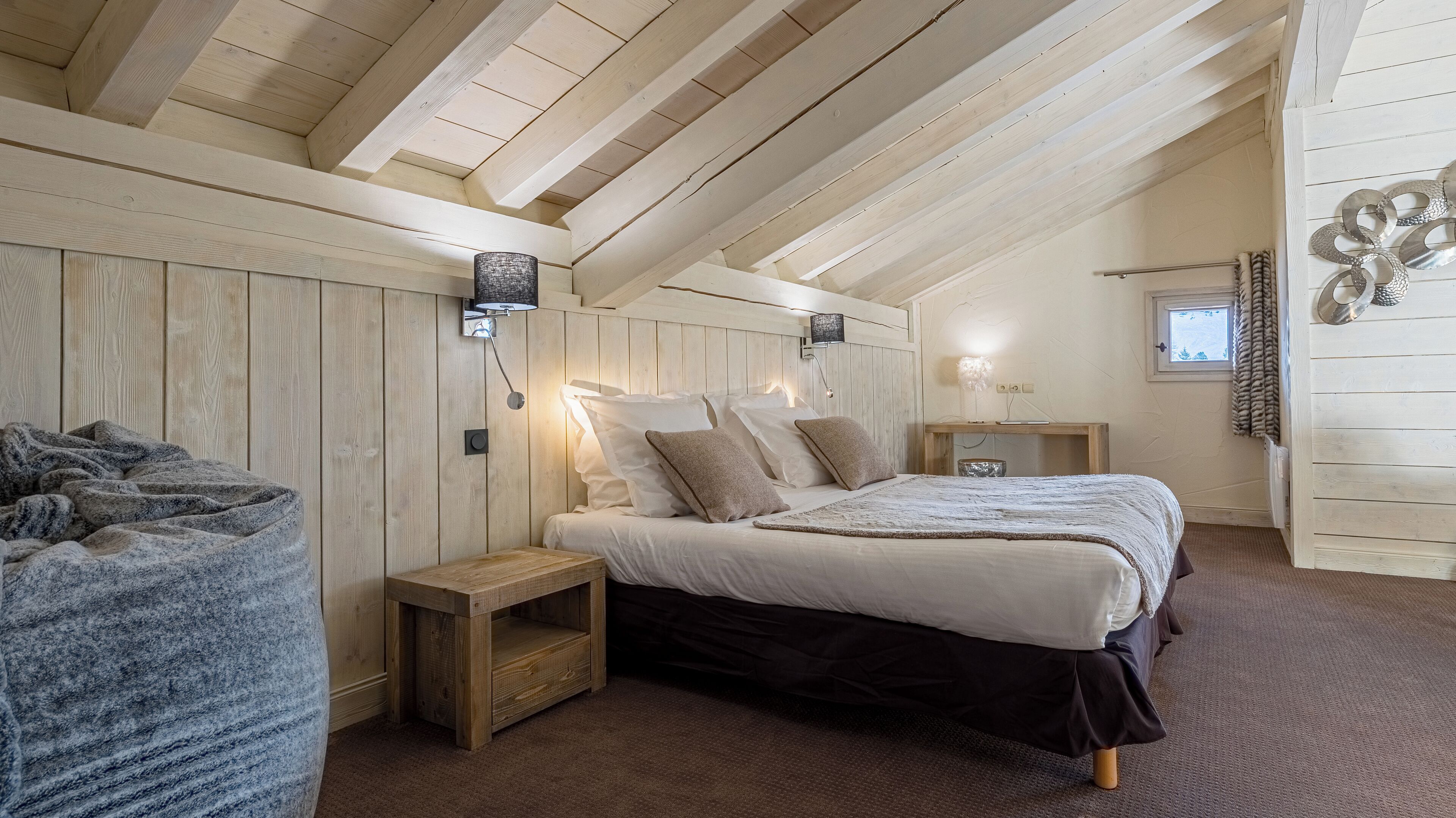 Une chambre confortable avec un plafond en bois, un lit avec une literie blanche et marron, une table de chevet et une petite table de nuit.