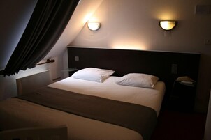 Quarto de hotel com cama, duas luminárias de cabeceira, mesa de cabeceira e janela com cortinas.