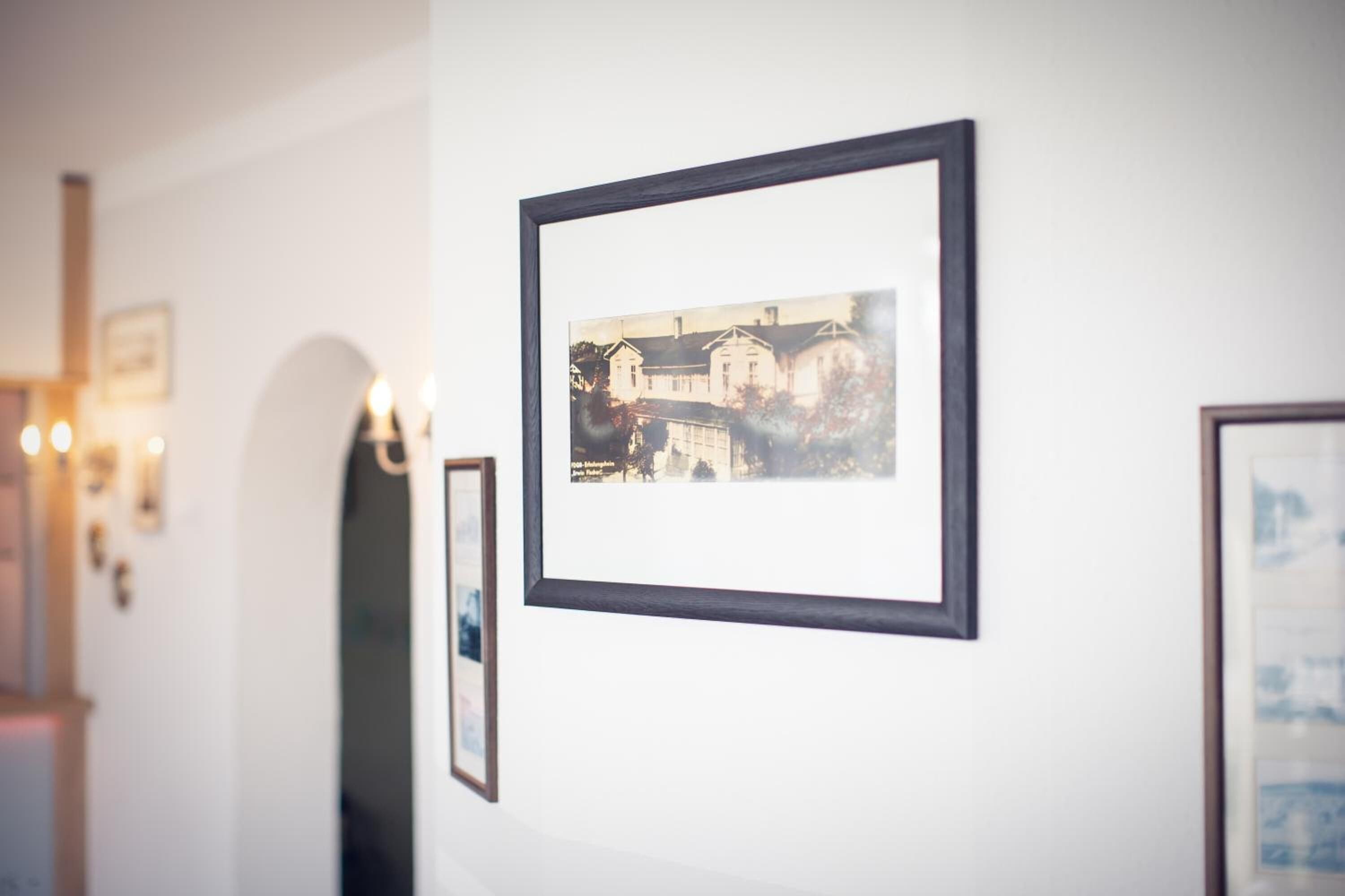 A hallway with framed photographs on the wall, a door with a mirror, and wall-mounted lights.