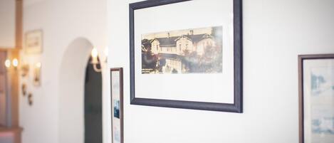 A hallway with framed photographs on the wall, a door with a mirror, and wall-mounted lights.