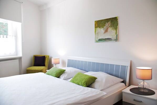 A hotel room with a bed, a chair, a nightstand, and a painting on the wall. - Appartementanlage-Ferienwohnungen Weiße Möwe (Sassnitz)