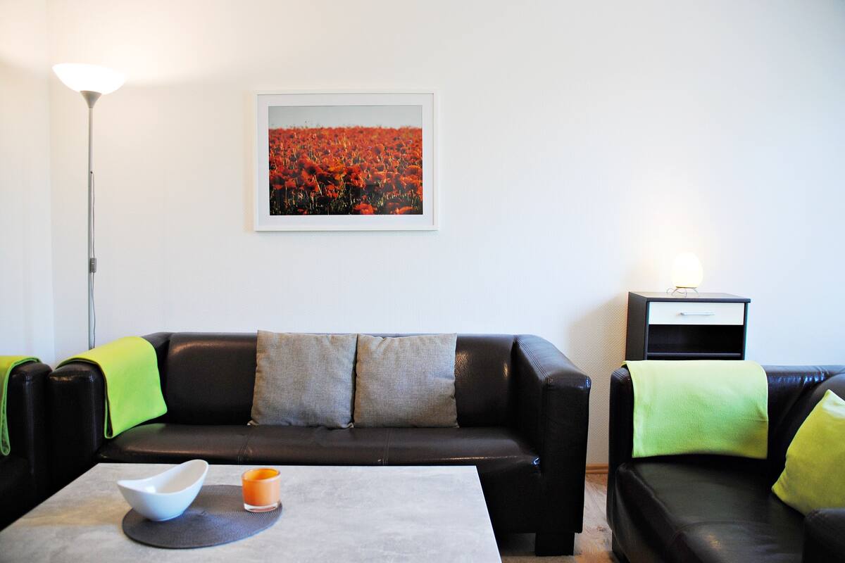 Ein Wohnzimmer mit einer schwarzen Ledersofa, einem Couchtisch und einem gerahmten Bild an der Wand.