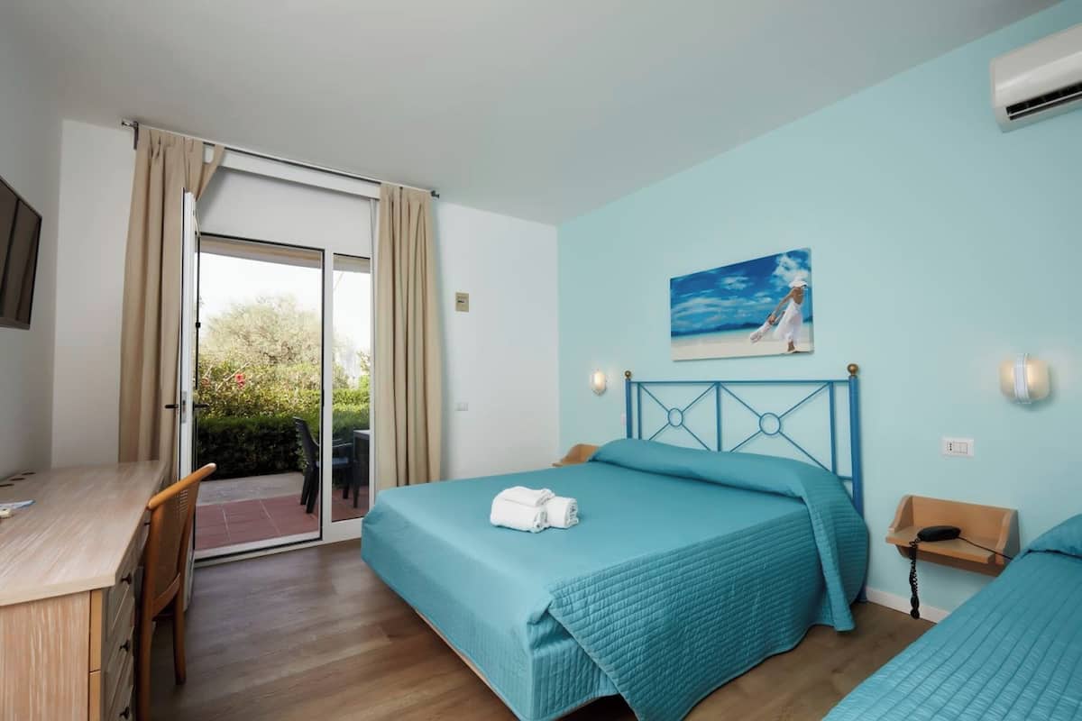 Ein Schlafzimmer mit zwei Betten, einem Schreibtisch und einem Stuhl. An der Wand hängt ein Bild und ein Klimagerät ist vorhanden.