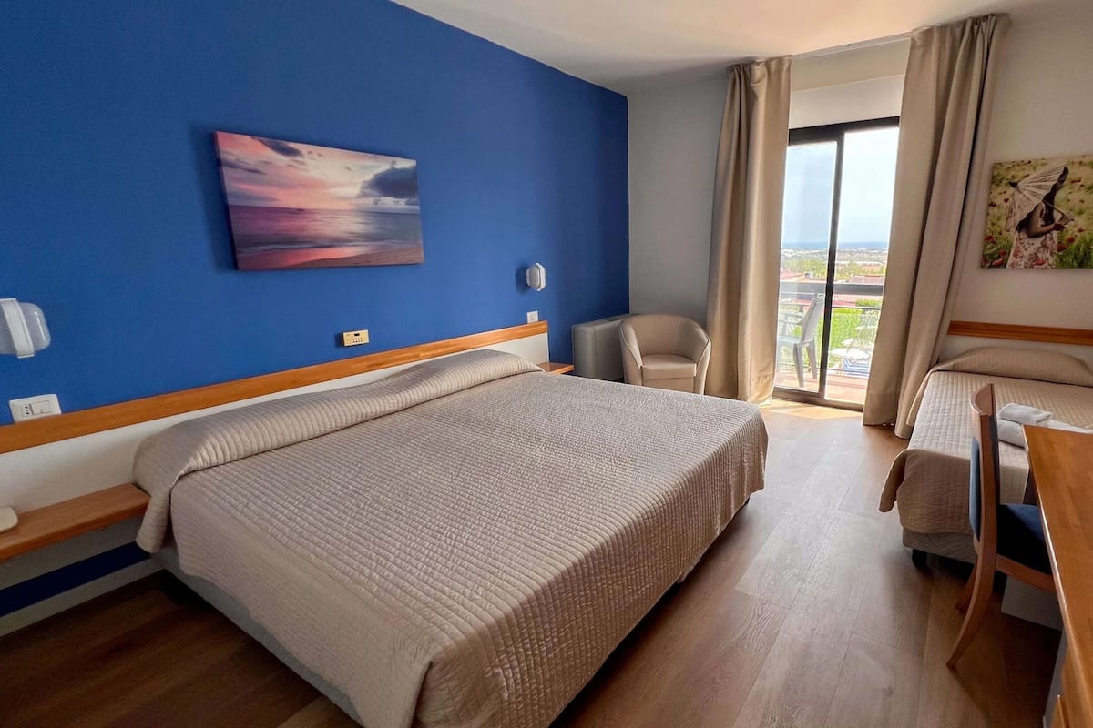 Ein Hotelzimmer mit einem großen Bett, einem Schreibtisch, einem Stuhl und einem Balkon mit Blick.