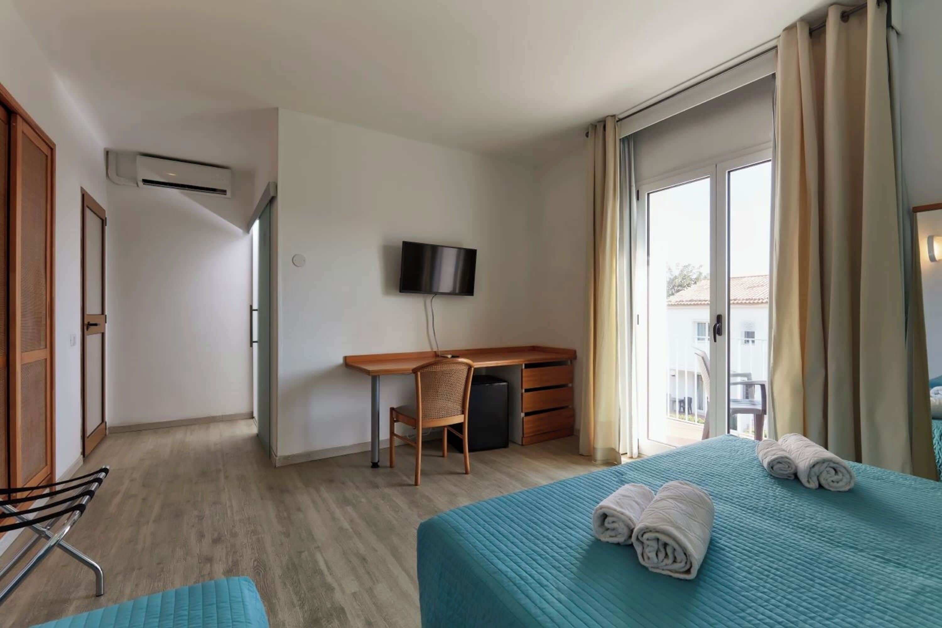 A hotel room with a bed, a desk, a chair, a TV, and a balcony.