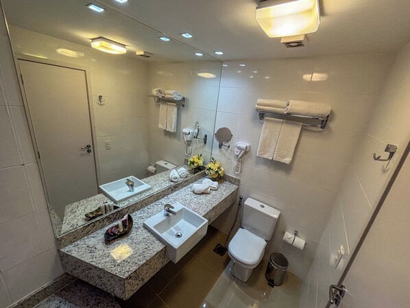 A modern bathroom with two sinks, a toilet, a trash can, and a mirror.