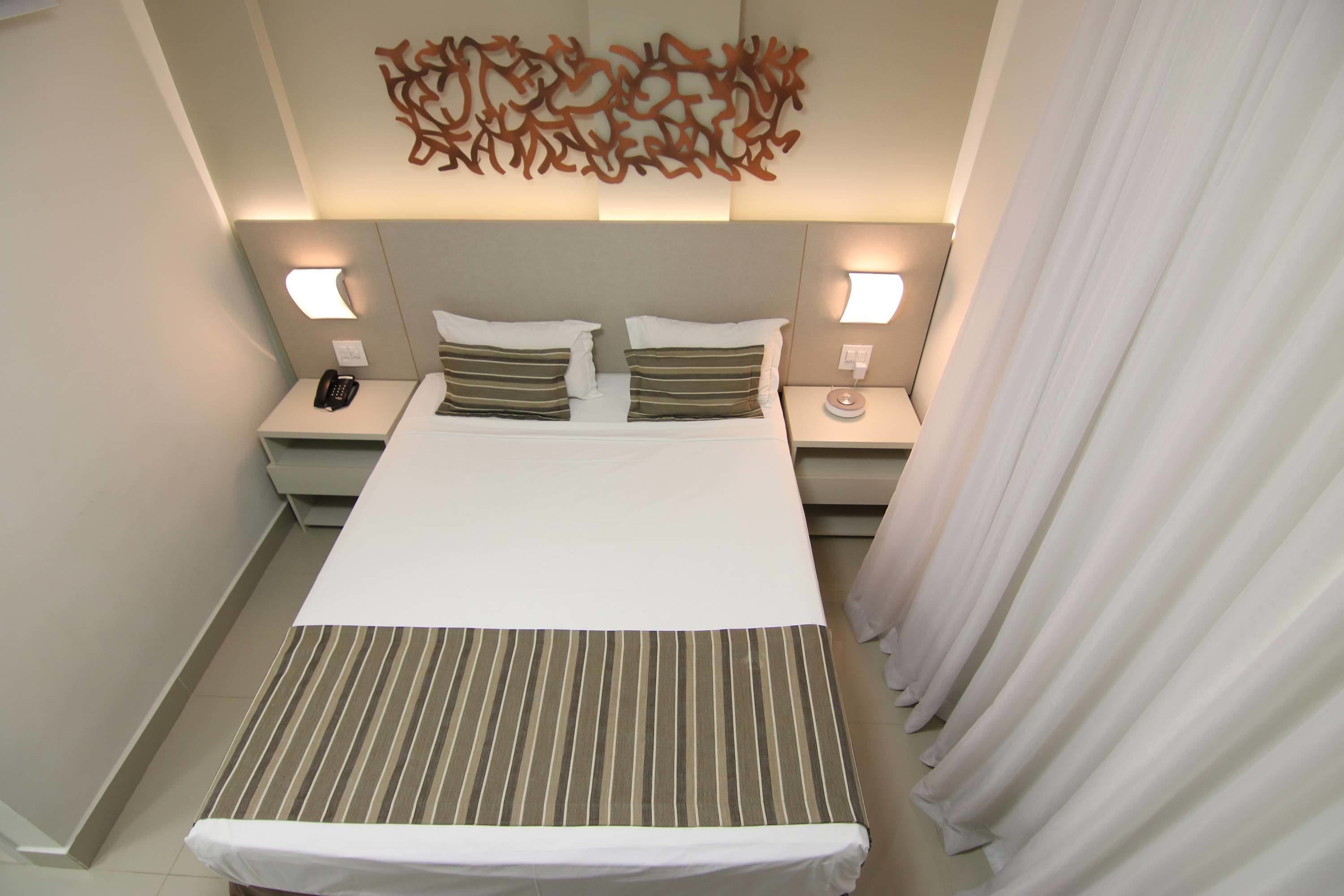 Camera d'albergo con un letto grande, due comodini, un quadro astratto appeso al muro e una tenda sul lato destro.