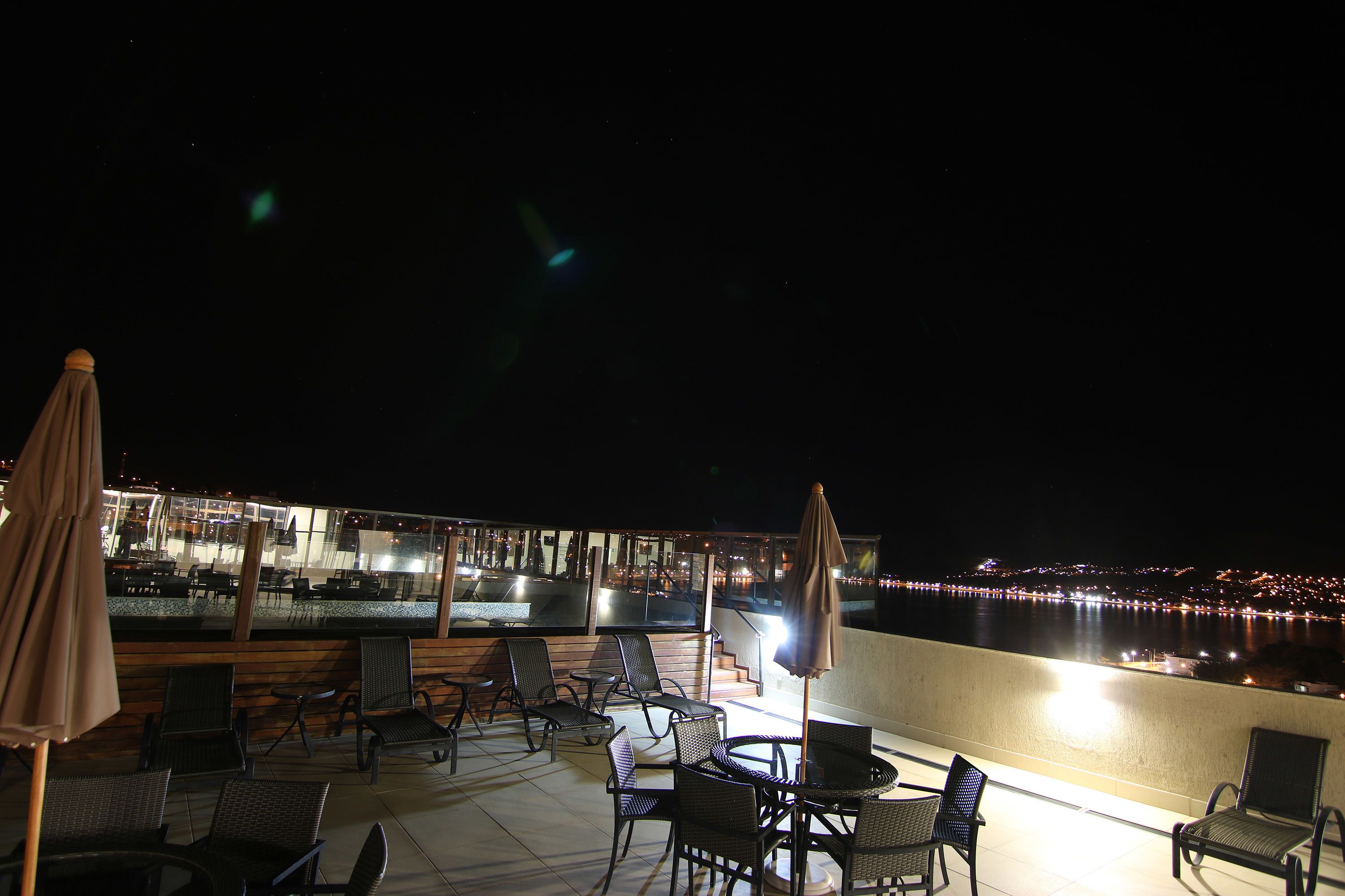 Une terrasse sur le toit avec des sièges en plein air, une vue sur les lumières de la ville qui scintillent au-dessus de l’eau et un espace bar.