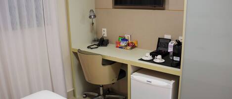 A hotel room with a desk, chair, and a small refrigerator.