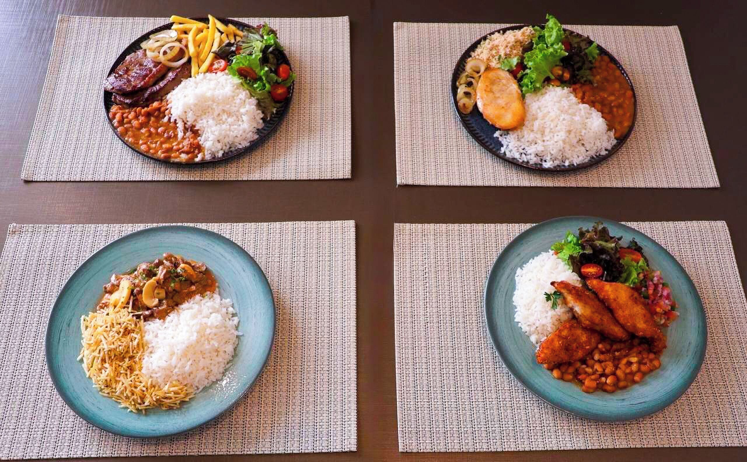 Four plates of food with rice, beans, and vegetables on a table.