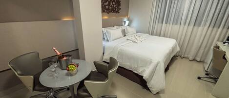 Ein Hotelzimmer mit einem Bett, einem Schreibtisch mit Stuhl, einem kleinen Tisch mit Flasche und Gläsern sowie einer Wanddekoration.