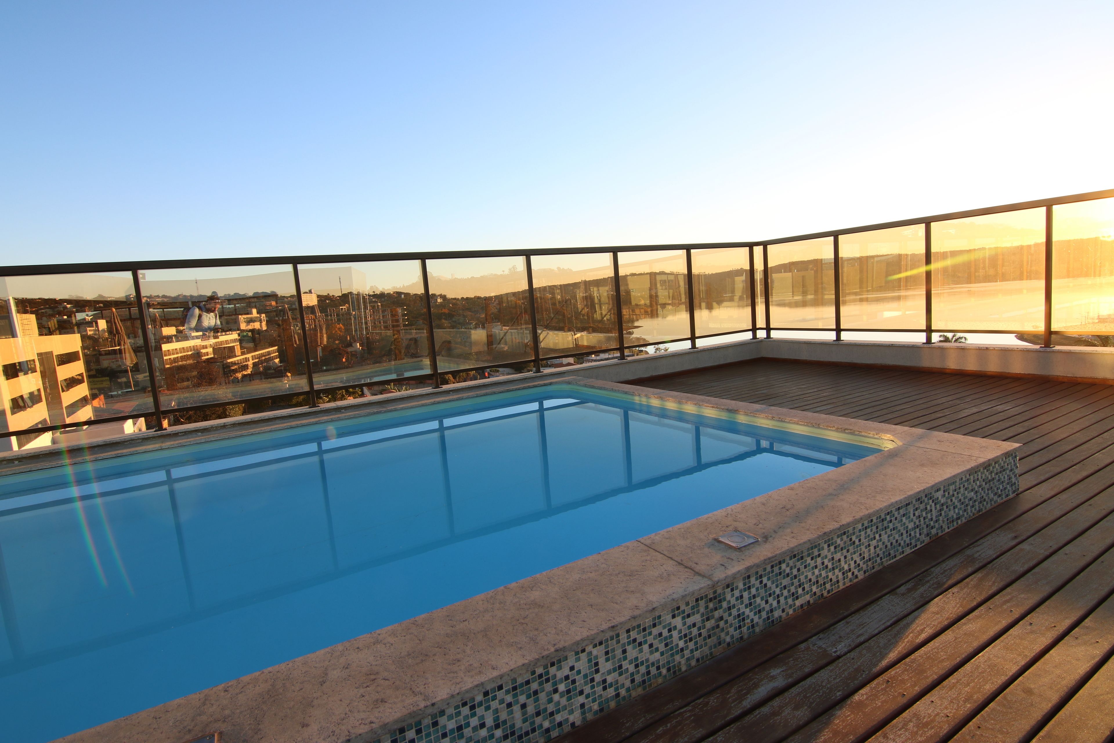 Una piscina en la azotea con vistas despejadas del paisaje urbano, rodeada por una barandilla de cristal.
