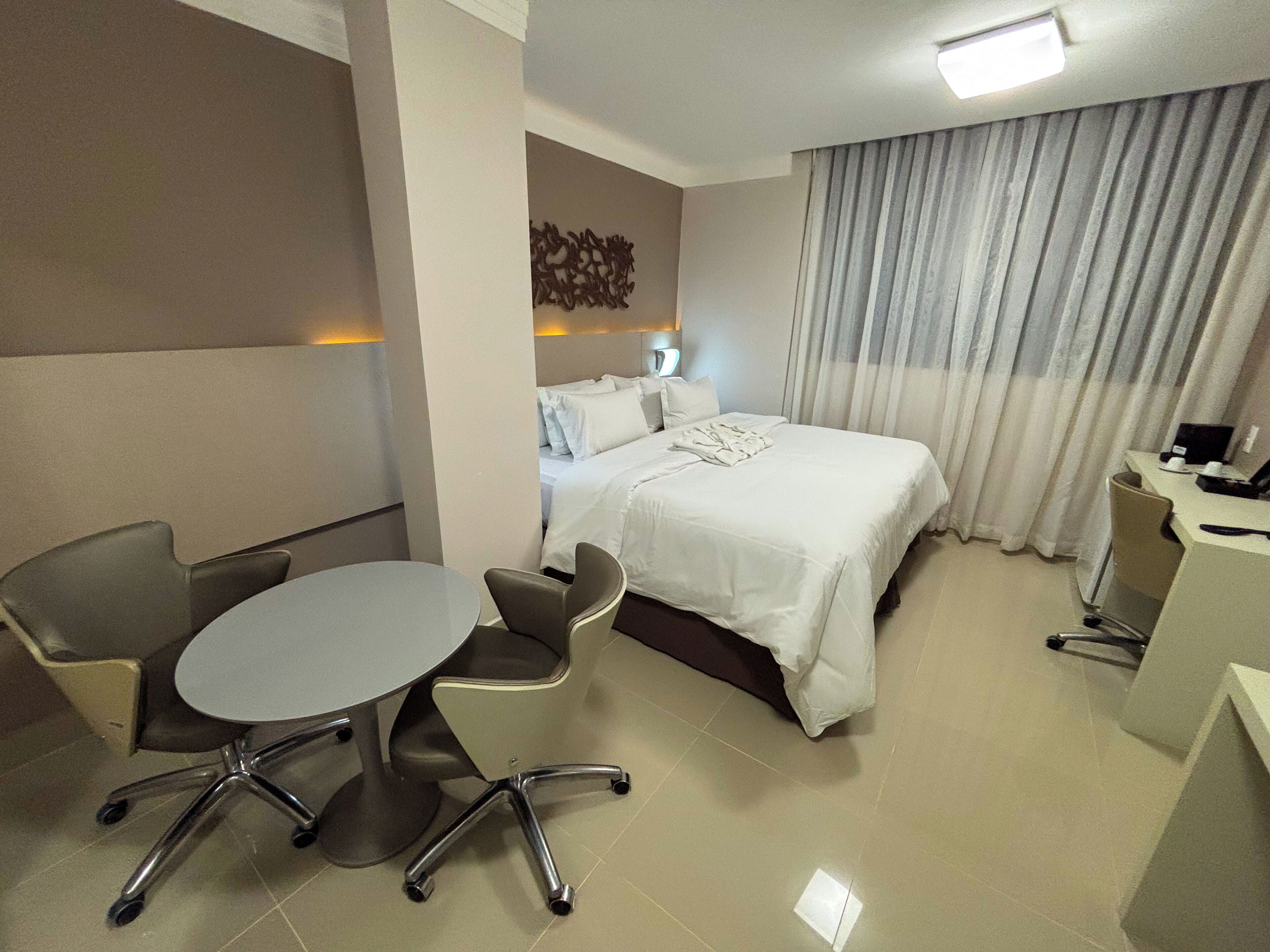 A hotel room with a bed, a desk, a chair, and a small table.
