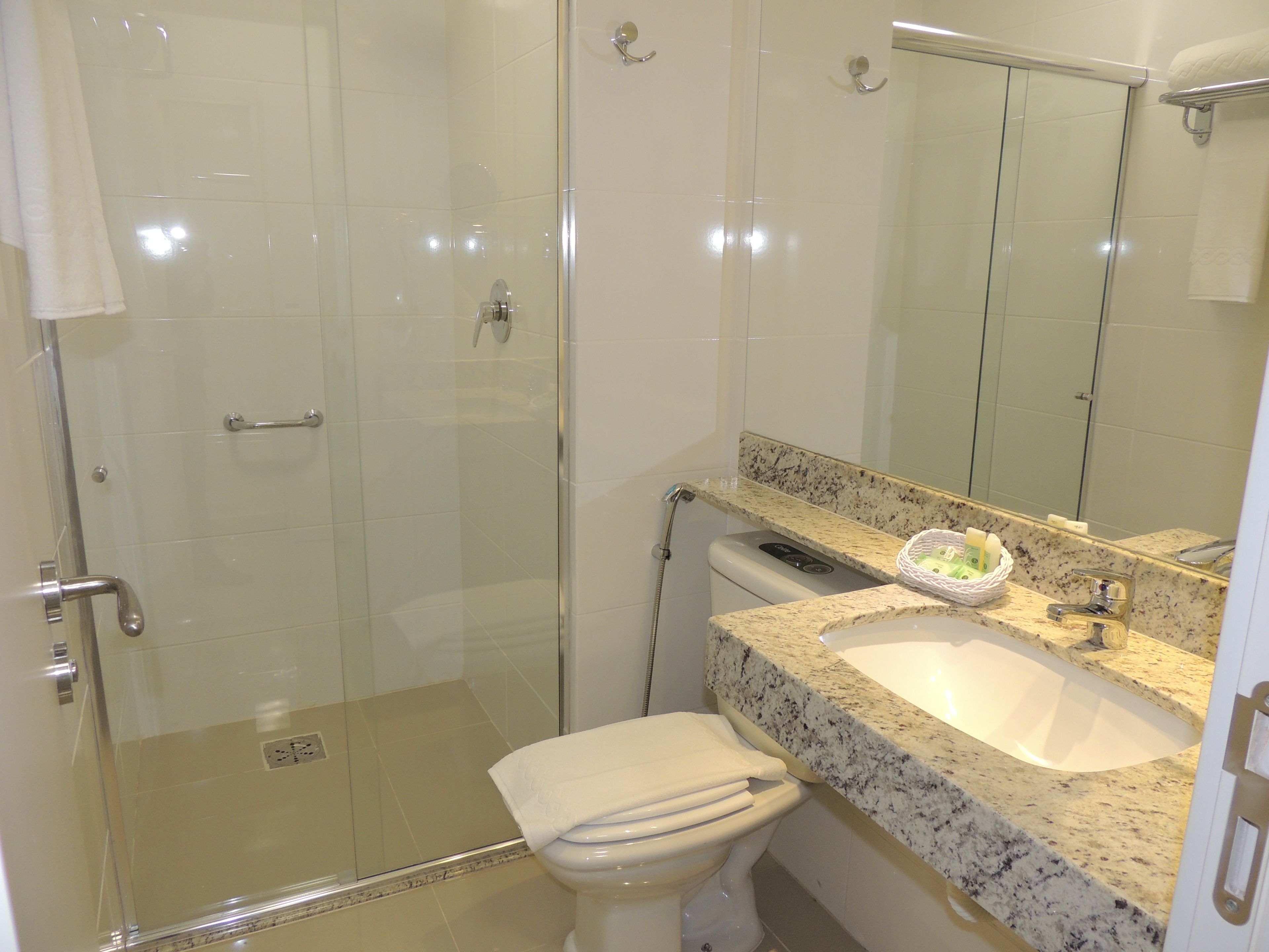 A bathroom with a glass shower enclosure, a white toilet, a granite countertop sink, and a mirror above the sink.