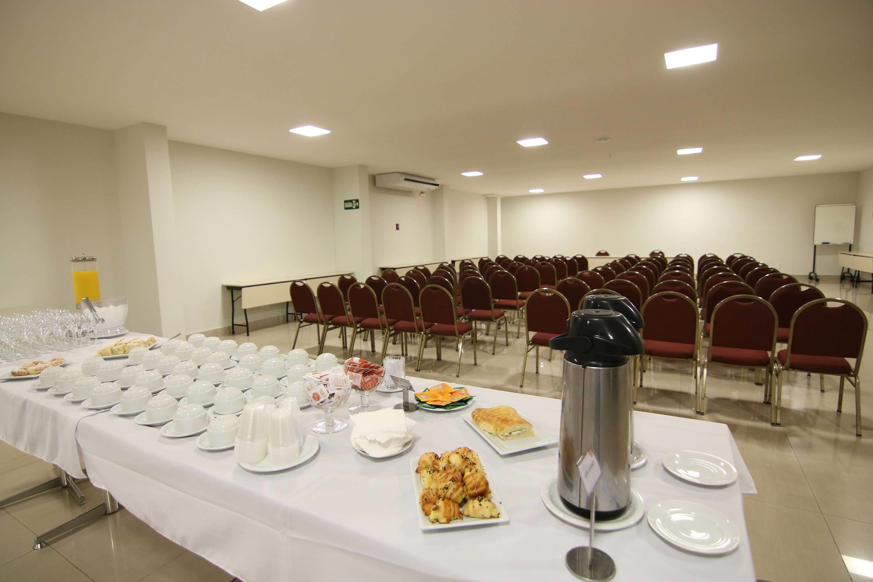 A conference room with rows of red chairs, a white table with food and drinks, and a whiteboard in the background.