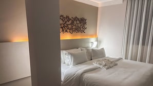 A hotel room with a neatly made bed, a modern chair, a wall art piece, and a large window with curtains. - Lagoon Prime Hotel (Lagoa Santa)
