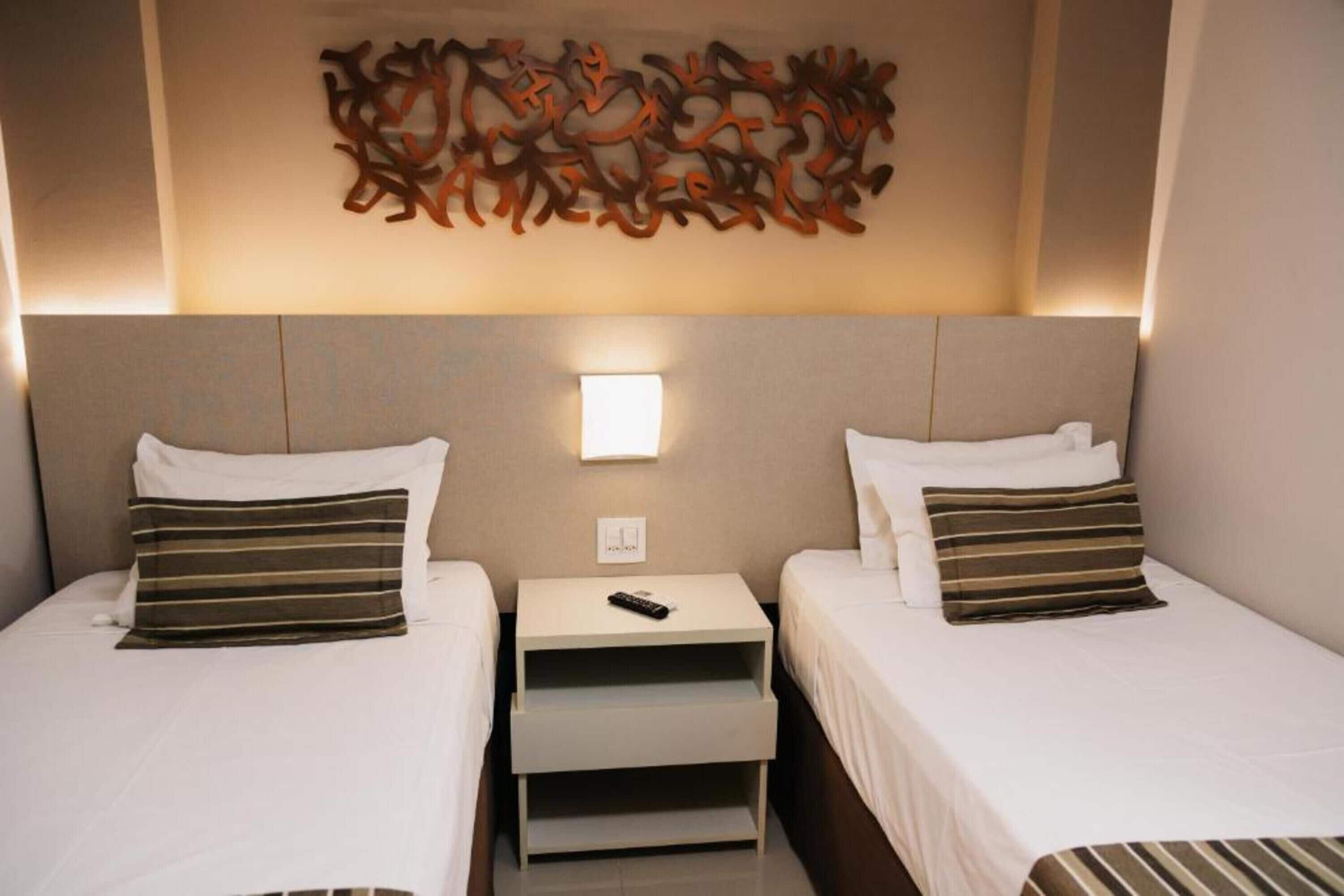 Une chambre d’hôtel avec deux lits, une table de chevet avec une télécommande et une œuvre d’art abstraite accrochée au mur.